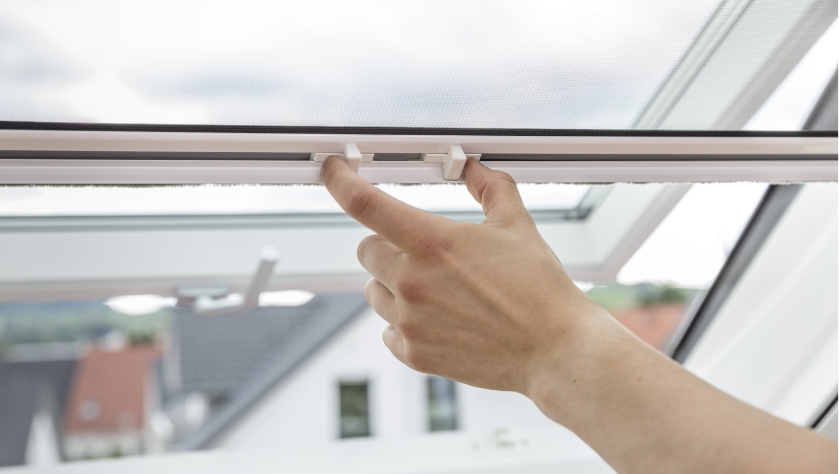 Nahaufnahme einer Hand, die ein Fliegengitter an einem Dachfenster öffnet.