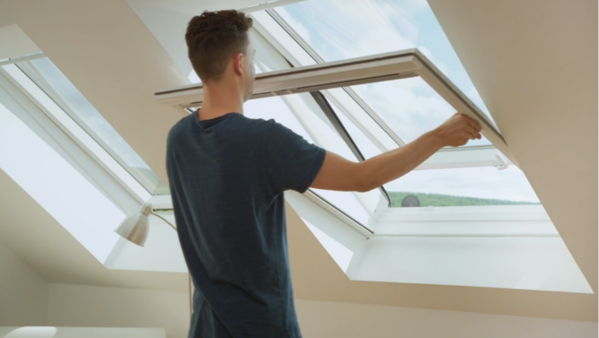 Mann zeigt, wie man ein Fliegengitter-Rollo an einem Dachfenster ein- und aushängt.